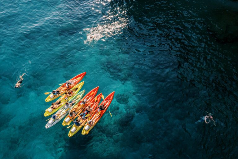 Tourists swim in the turquoise sea near a team of kayakers in kayaks